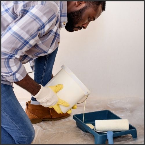 male pouring paint from a bucket into a paint tray, getting ready to paint the walls of the interior of his home