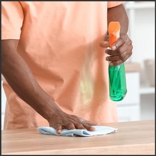 male wiping down counter top with blue microfibre cloth and cleaner