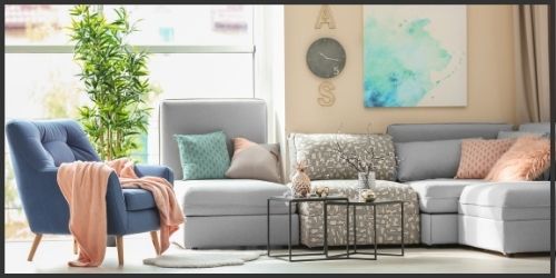 living space with beige walls, gray couch, and timeless accents of pink, navy, and green/blue.